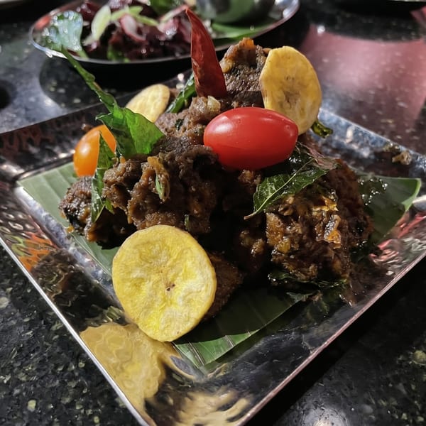 Close-up of a dark, savory dish garnished with cherry tomatoes, banana chips, and a red chili.