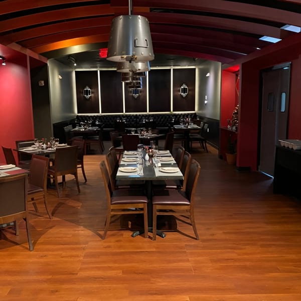 Restaurant dining room with red walls, wooden floors, set tables, and dark booths along the back wall.